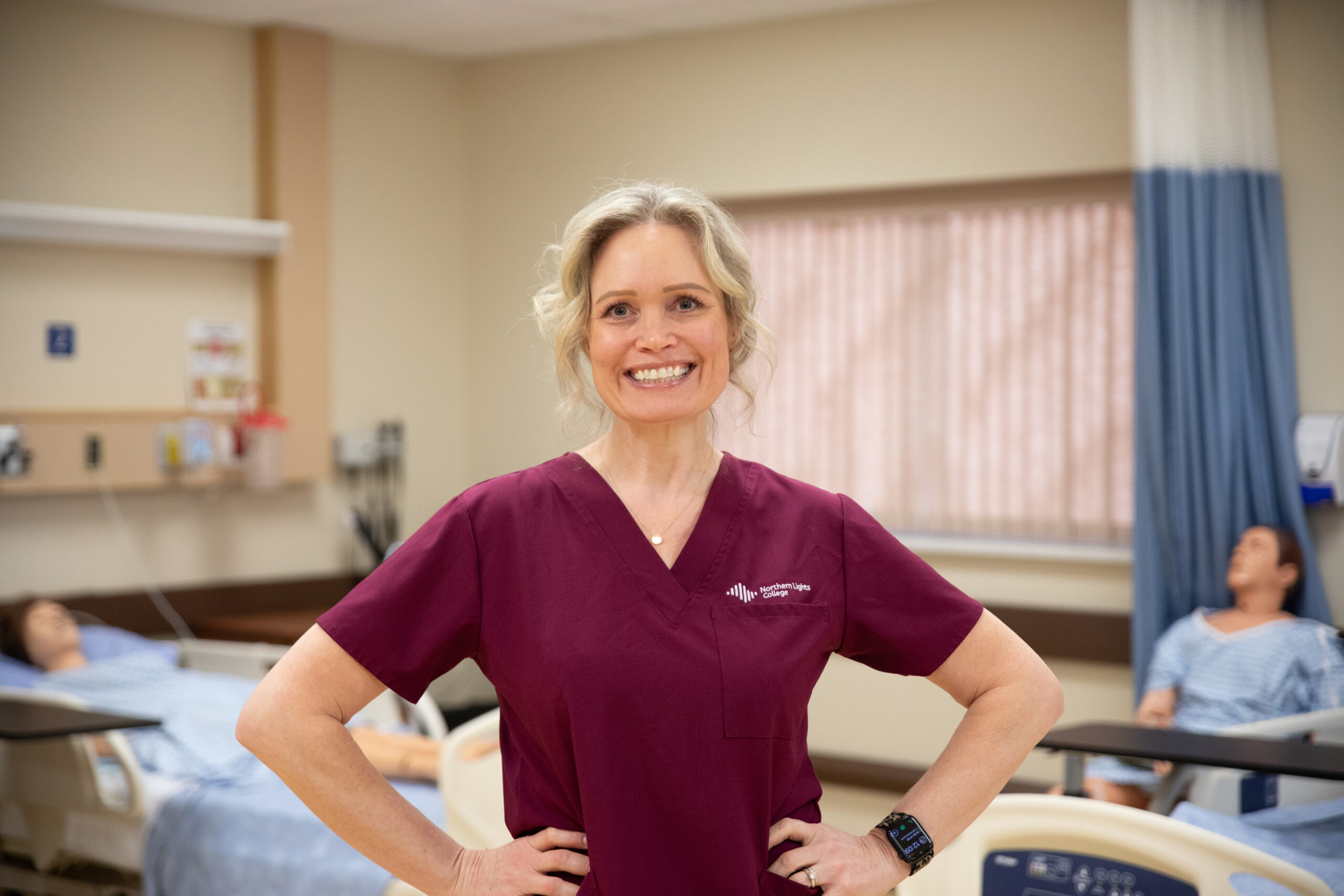 April Trasy stands in the nursing lab wearing burgundy scrubs