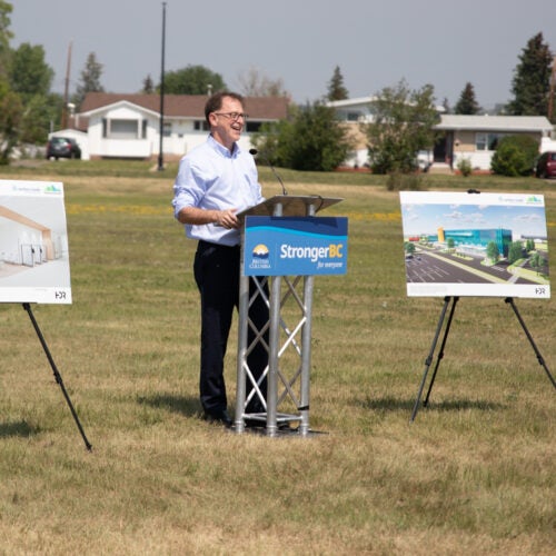 BC Health Minister Adrian Dix speaks from a podium flanked by two artists' renderings of the new Dawson Creek Hospital.