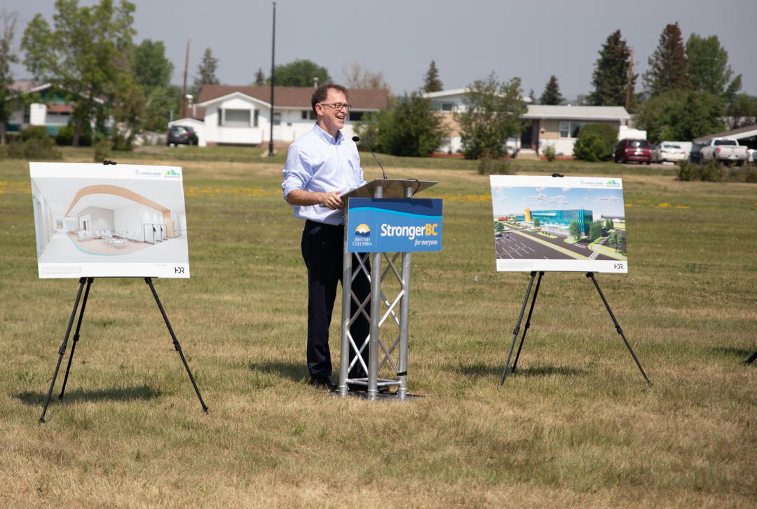BC Health Minister Adrian Dix speaks from a podium flanked by two artists' renderings of the new Dawson Creek Hospital.