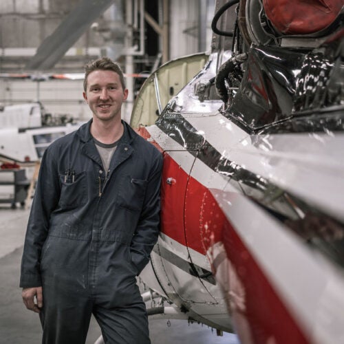 AMT student Bryce Brown stands next to a helicopter in the AMT hangar