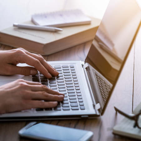 person's hands working on keyboard with books, pen and glasses
