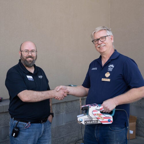 Co-op manager shakes hands with NLC instructor who is holding a belt sander