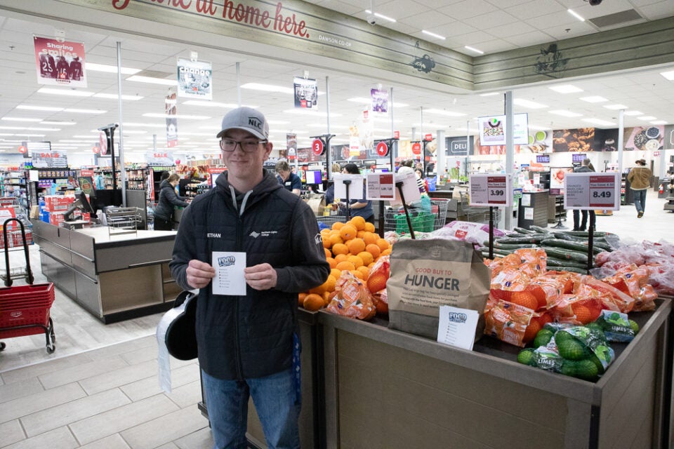 A student stands holding a sign in the grocery store