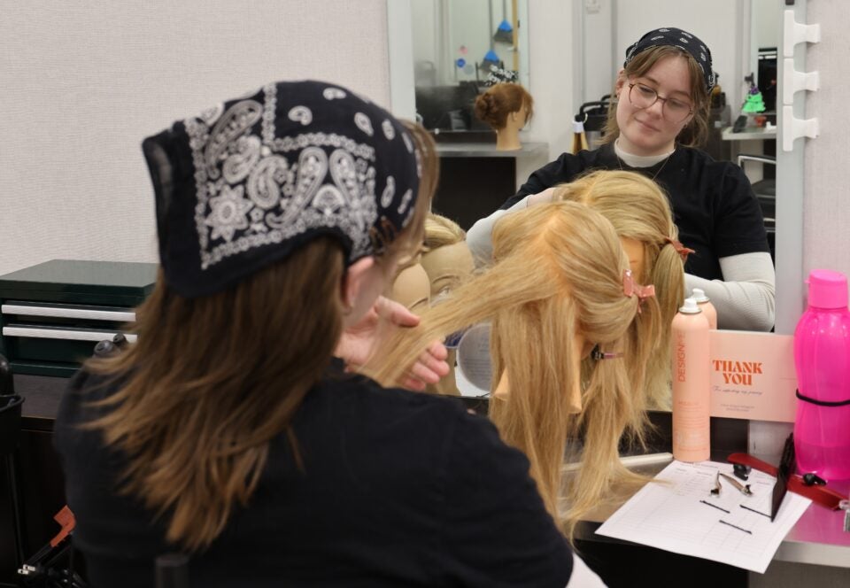 A student styles the hair on a model head