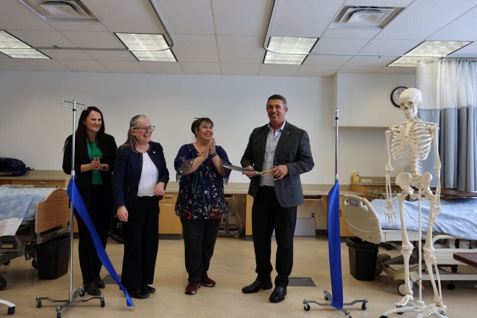 Todd Bondaroff stands with large scissors after cutting the ribbon. Three people cheer him on