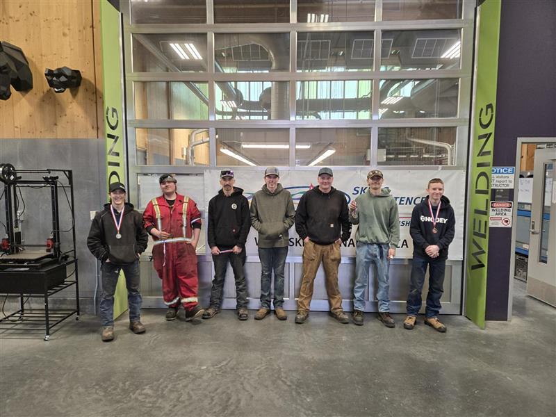 Welding students stand in a line wearing medals