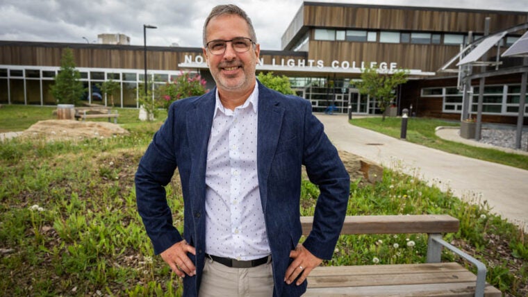 A man in a blue blazer stands in front of the entrance to Northern Lights College.