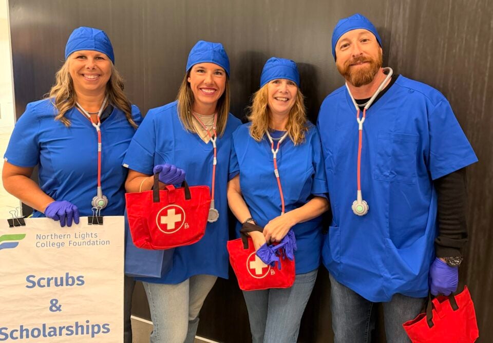 People dressed in blue scrubs smile holding a sign that says scrubs and scholarships