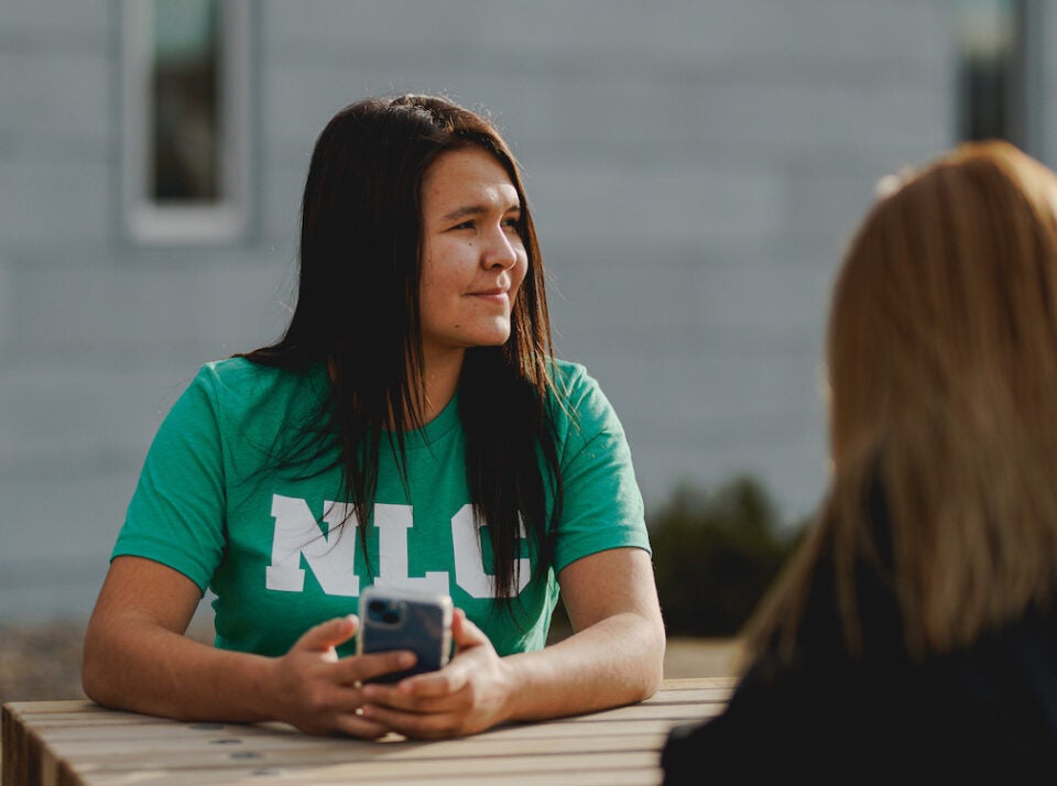 NLC student sitting at a picnic table in an NLC branded t-shirt