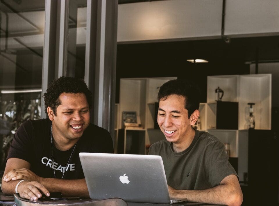 Two friends laughing and looking at laptop