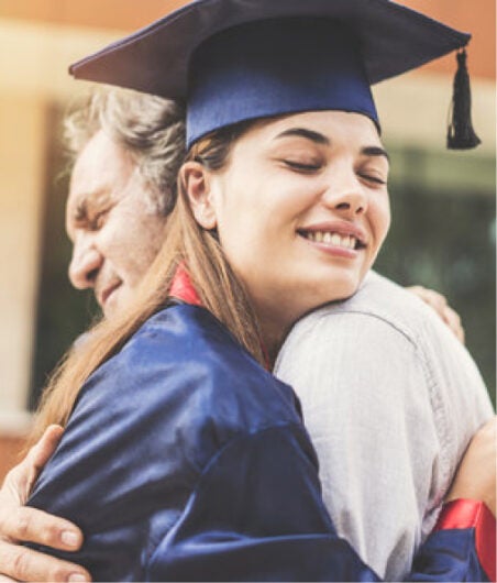 Young woman in graduation gown hugging her father at NLC graduation