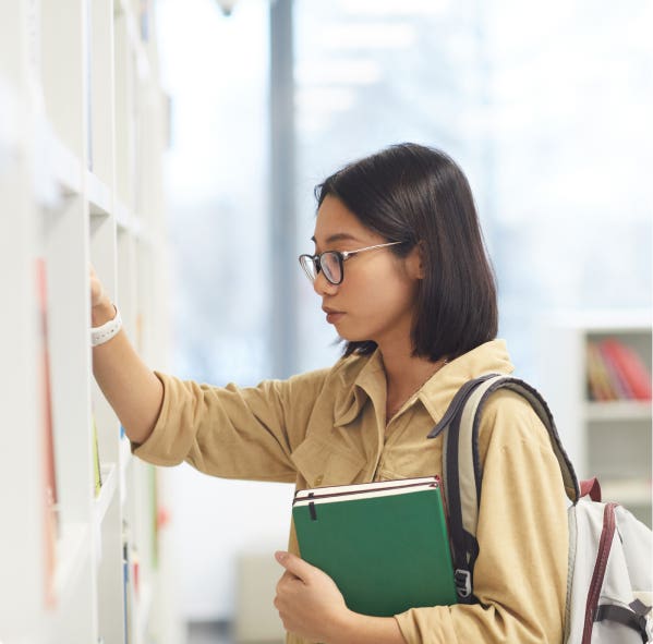 Student looking at books on library shelf